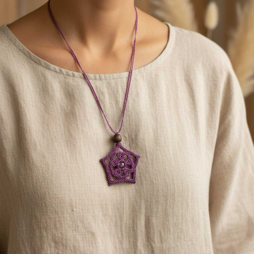 Sautoir Cassiopée en micro-macramé améthyste avec pendentif floral étoilé et perle centrale améthyste, porté sur tunique beige, vue de face